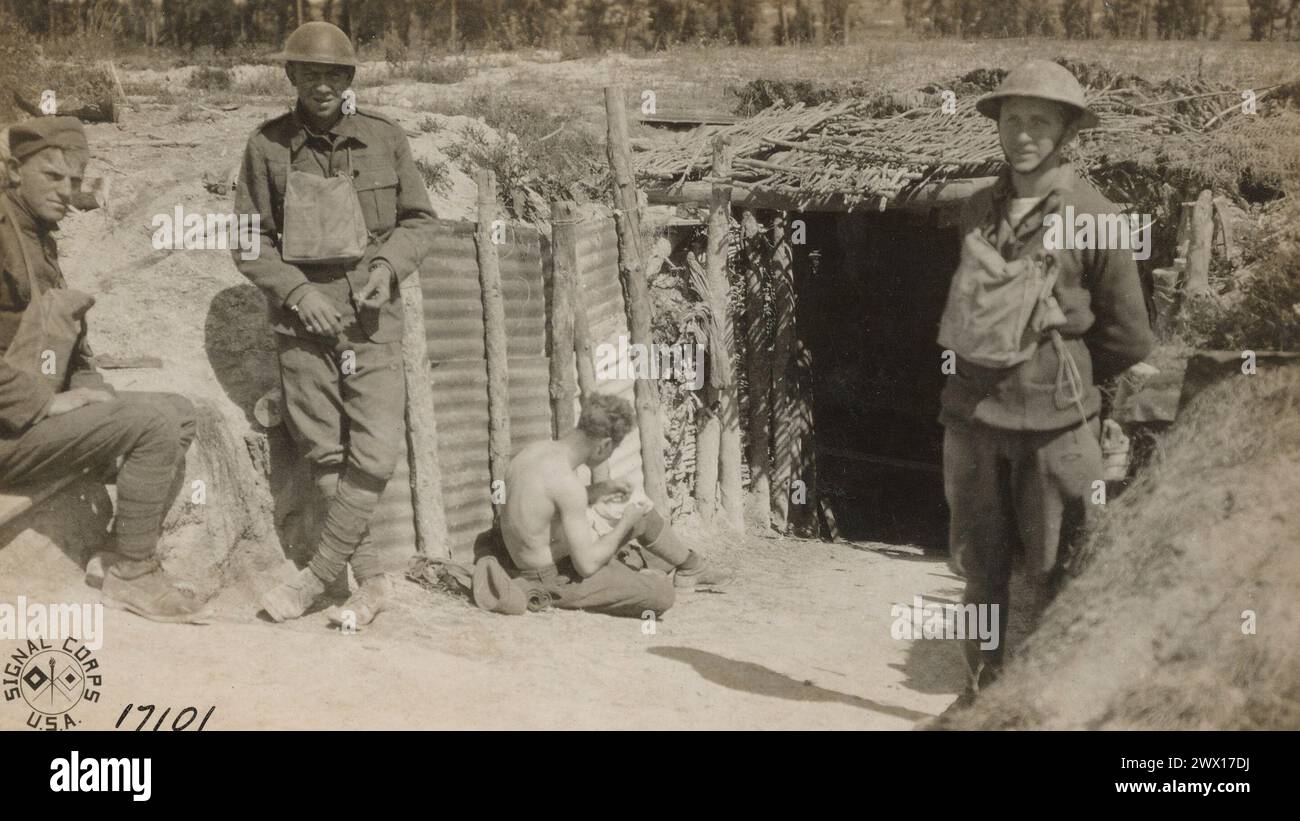 A member of the 166th Infantry picks cooties out of his shirt at the door of a dugout near 2nd line trenches west of Suippes France ca. 1918 Stock Photo
