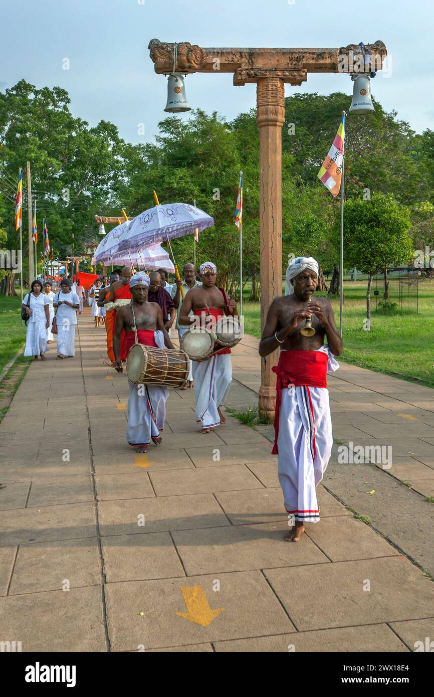 A trumpet blower leads a procession of Buddhist monks walking towards