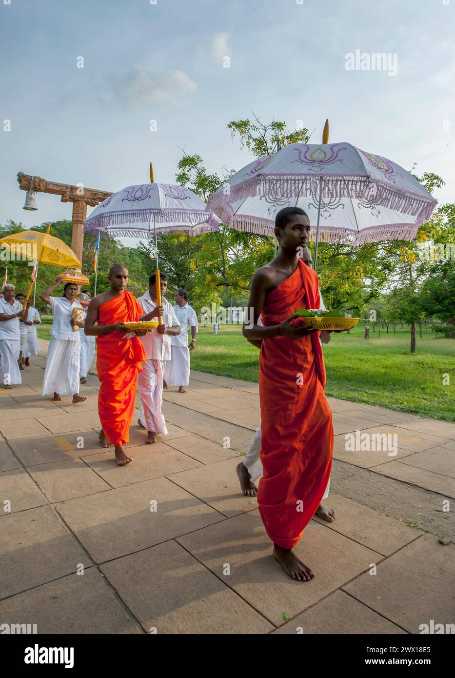 Buddhist monks shielded by umbrellas from the afternoon sun carry offerings towards the Ruwanwelisaya Dagoba at Anuradhapura in Sri Lanka. Stock Photo