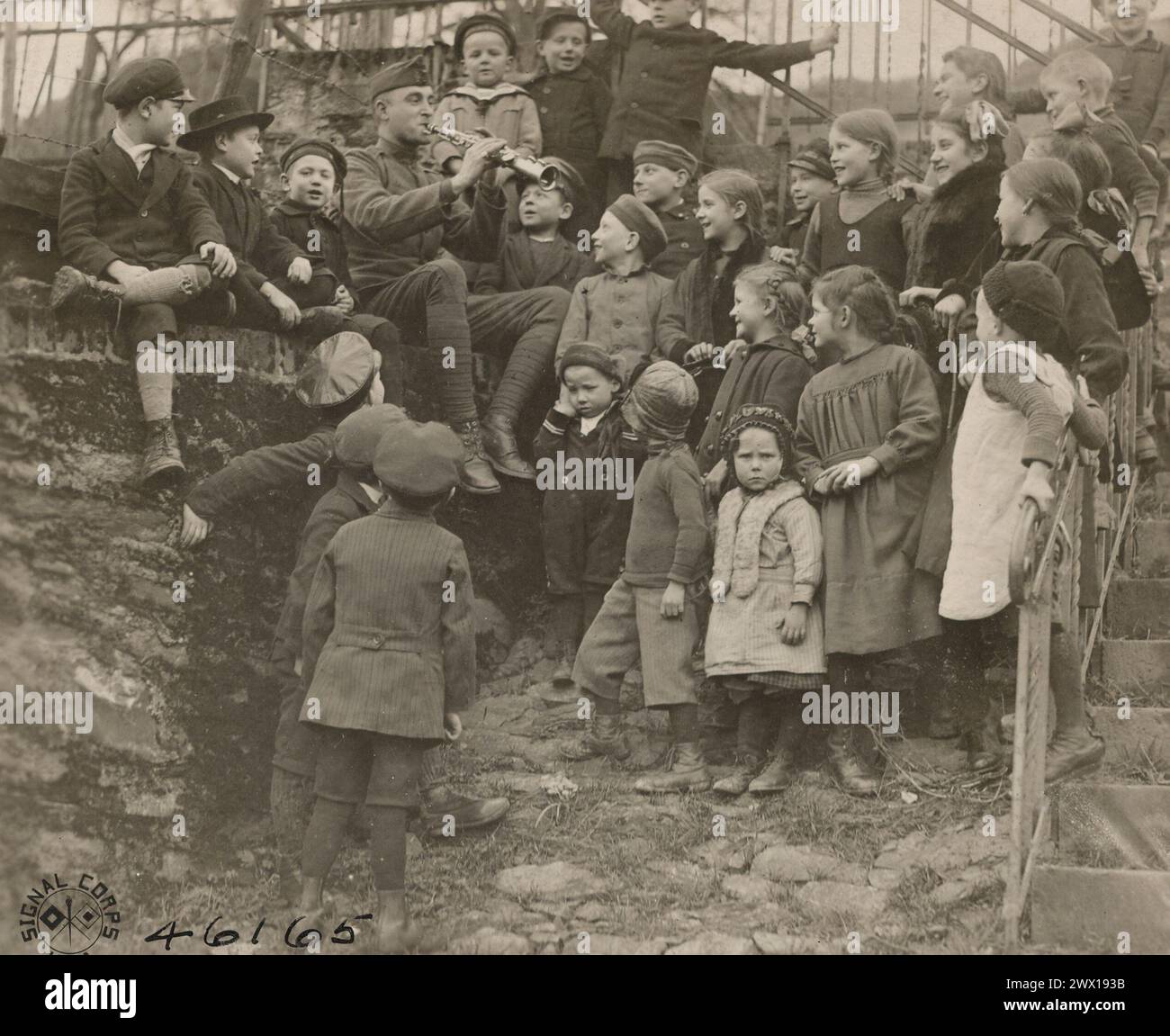 MUSICIAN JOE FOSTER OF THE 51st Infantry Band, 4th Army Corps, teaching German children American songs. He is seated on a wall in one of the village streets and children are grouped about him singing. Cochem, Germany ca. 1919 Stock Photo