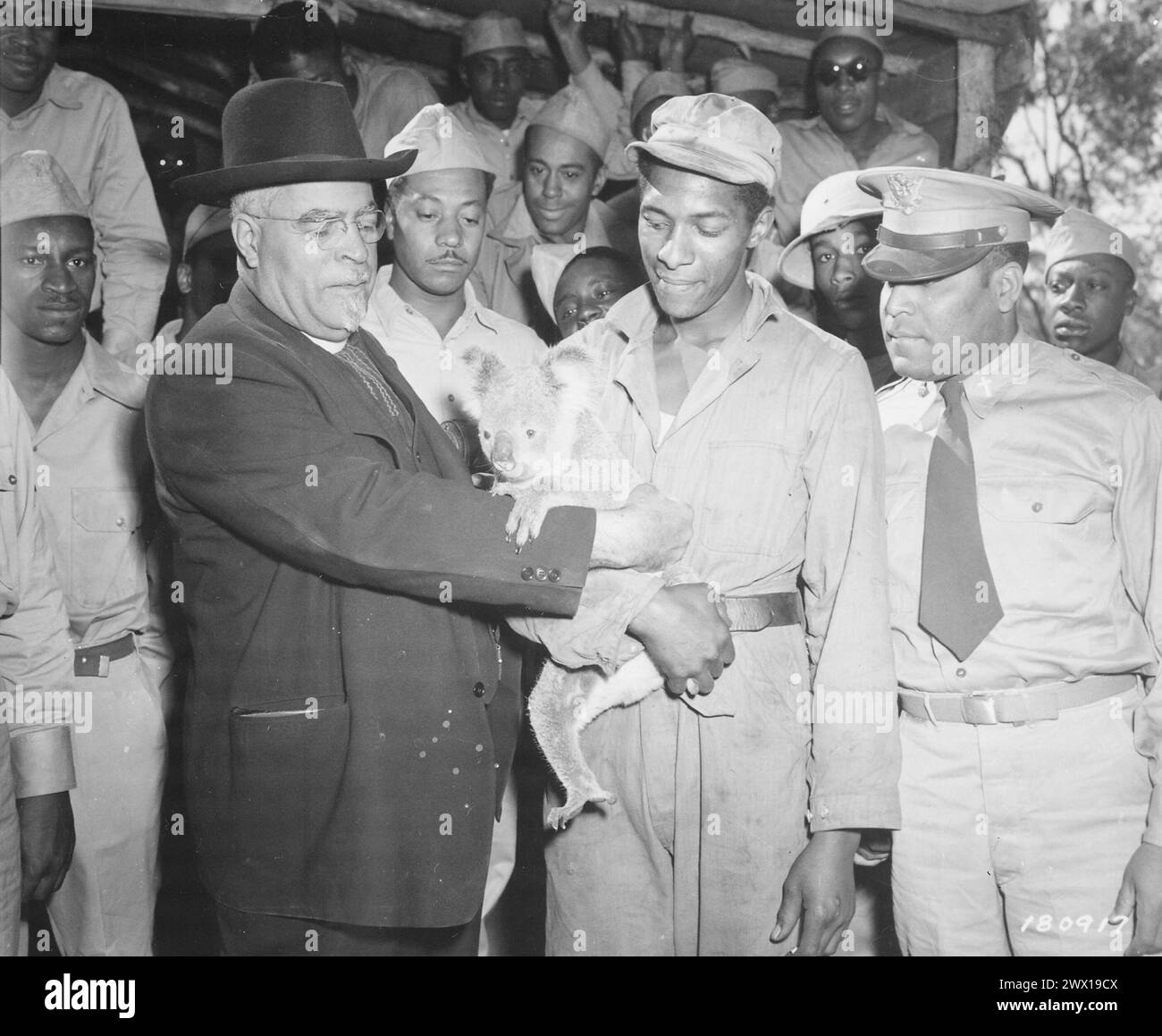 Bishop John Andrew Gregg, Leader of [the] African Methodist Church in North Central United States and Envoy of President Roosevelt, fondles a pet koala bear adopted by Pfc. Sammy Hurt... Around the Bishop are members of the [630th] Ordnance Company ca. 1943 Stock Photo