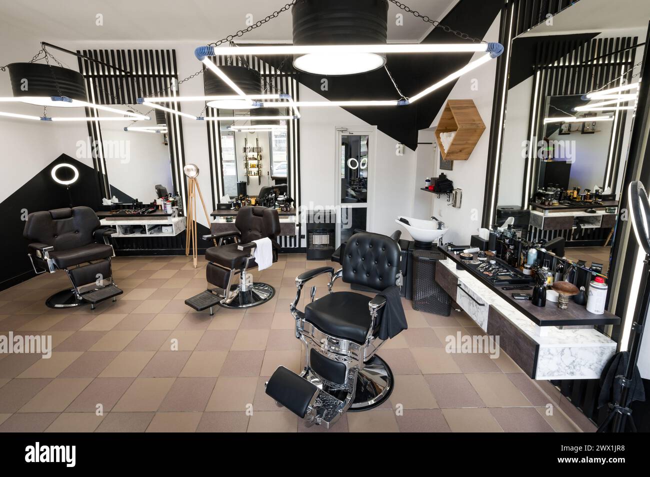 The modern interior of a men's barbershop with chairs is shot at a wide angle. Designer interior of a hair salon in black and white colors with LED la Stock Photo