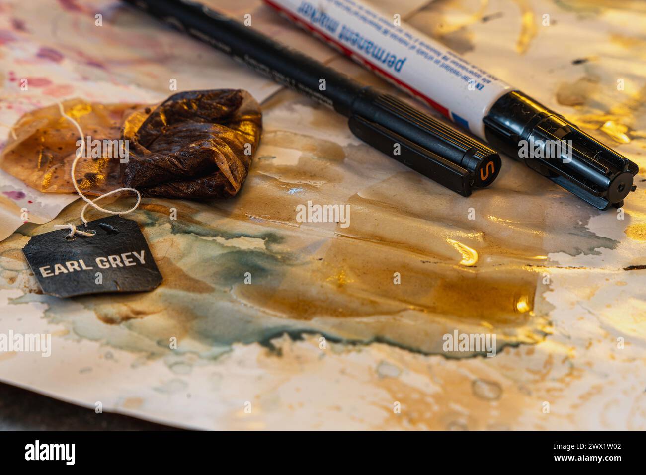 High angle of used teabag with thread connecting to black tag with letters earl grey while spread tea water on messy sheet with color smudges and mark Stock Photo