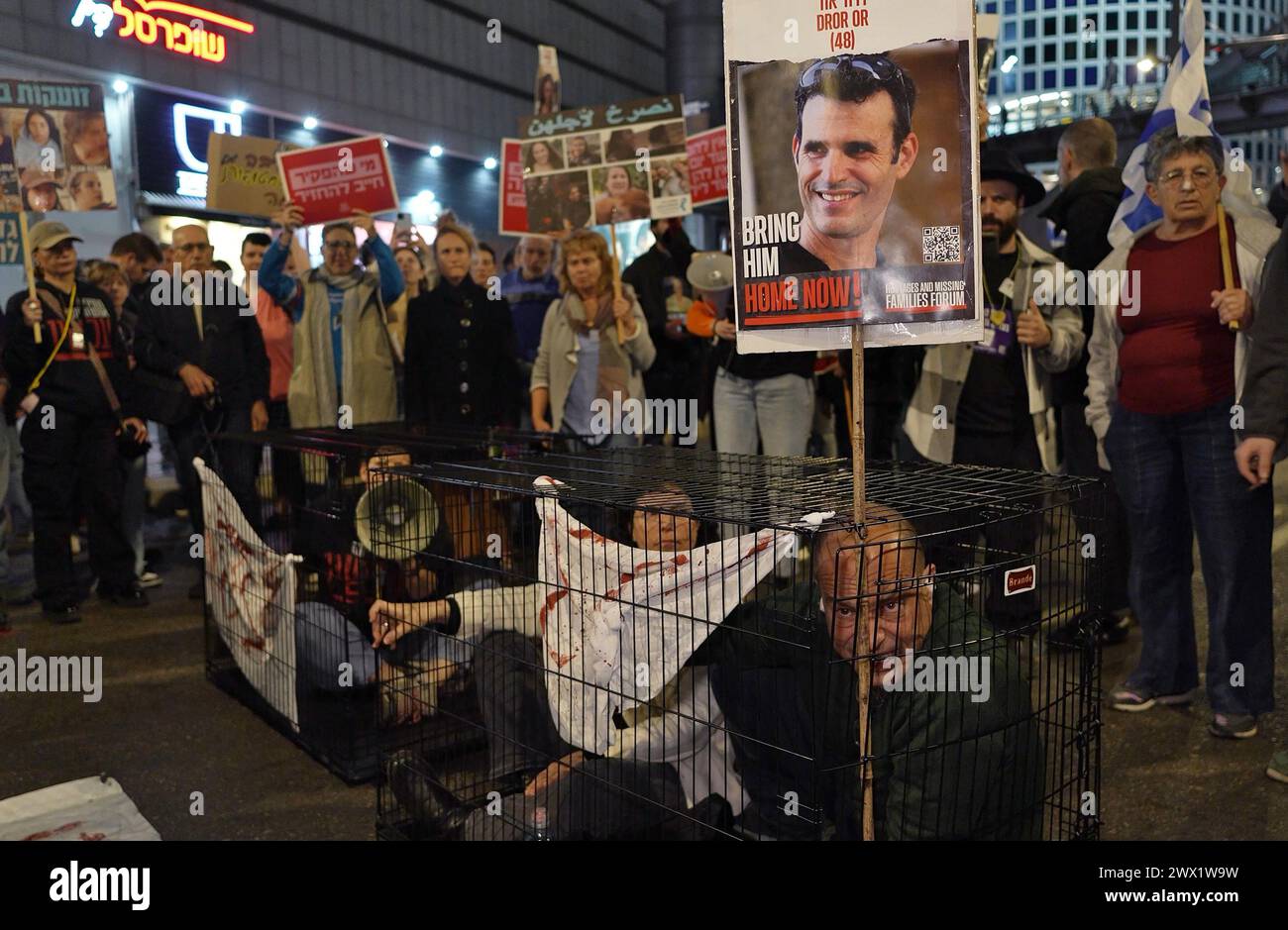 Family members of the hostages still in Gaza sit in cages to represent their loved ones, as they block a major motorway outside the Defense Ministry during a demonstration after the collapse of the latest round of hostage negotiations in Qatar and calling for a deal to free Israeli hostages held in the Gaza Strip on March 26, 2024 in Tel Aviv, Israel. Stock Photo