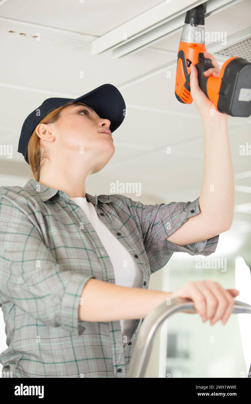 woman using cordless drill on ceiling Stock Photo