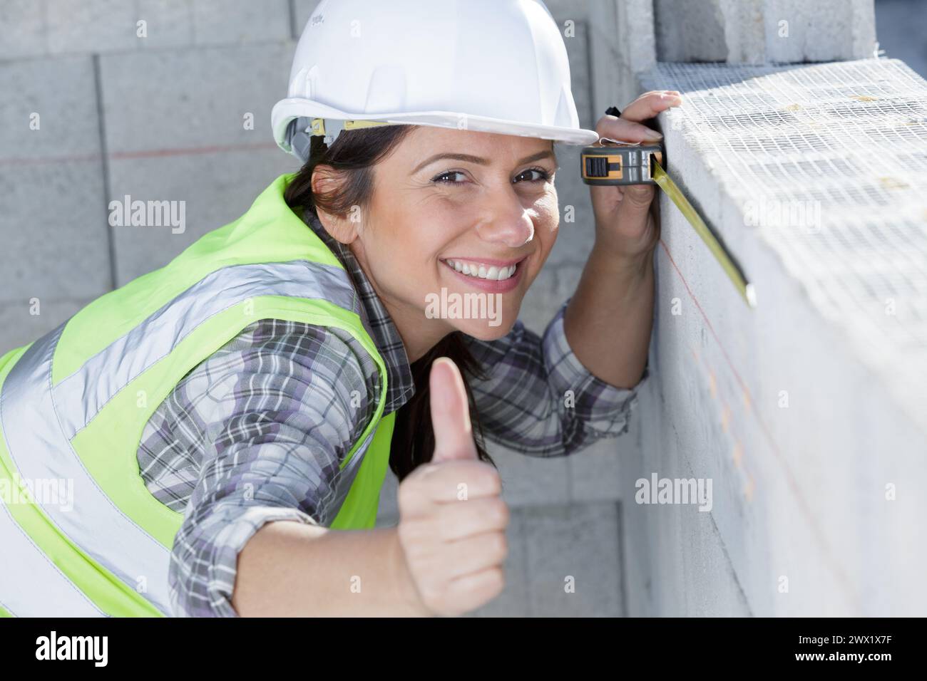 happy female builder showing thumb-up while measuring a wall Stock Photo