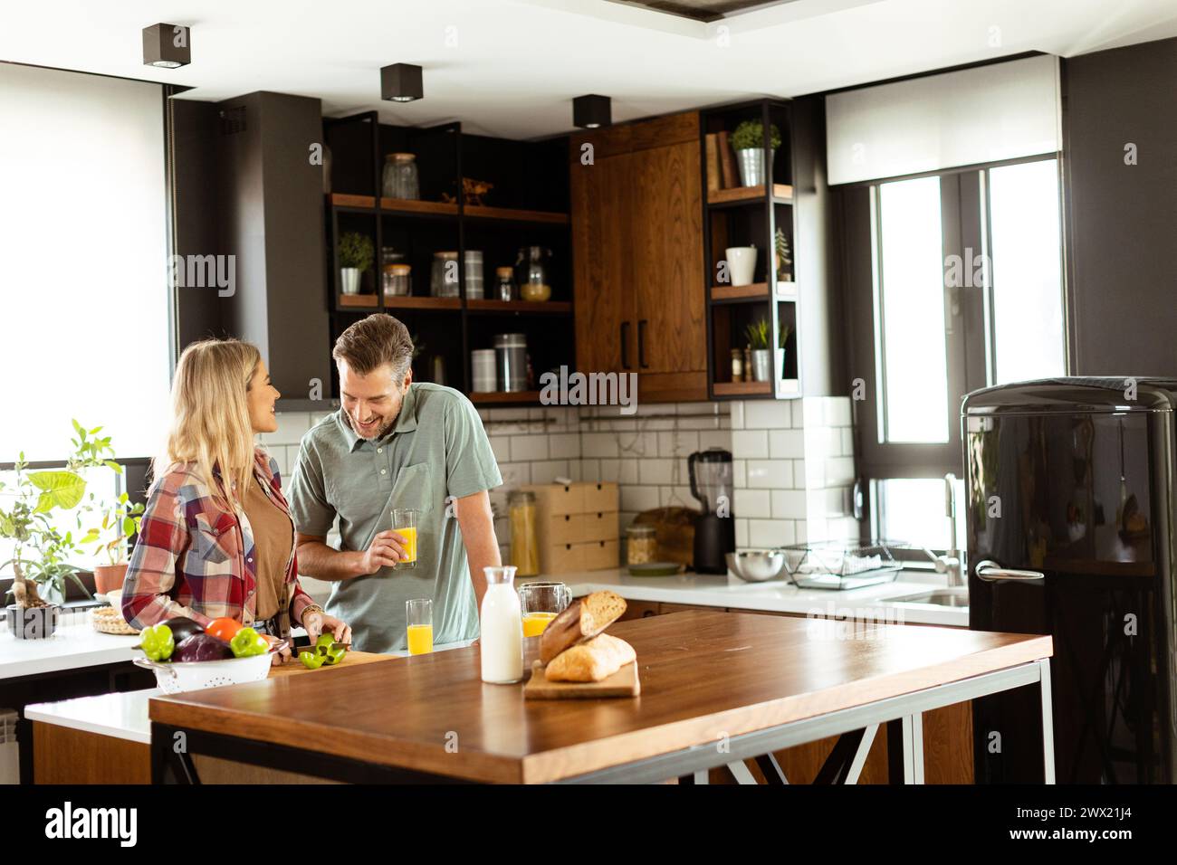 A pair enjoying a lighthearted conversation with fresh juice and a healthy breakfast spread on the counter. Stock Photo