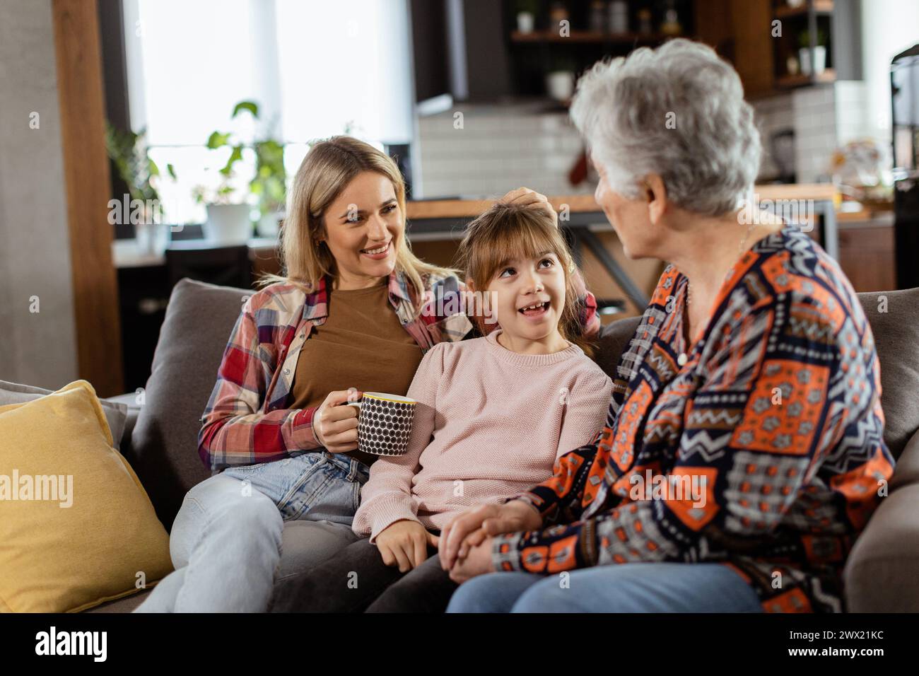 Three generations of women enjoy laughter and conversation on a comfortable living room couch Stock Photo