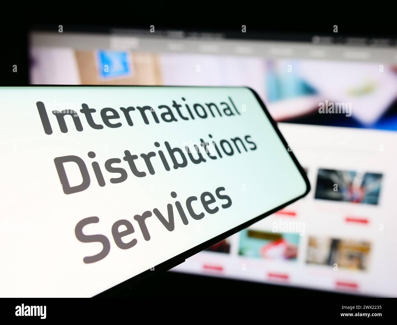 Smartphone with logo of British company International Distributions Services plc in front of website. Focus on center-left of phone display. Stock Photo