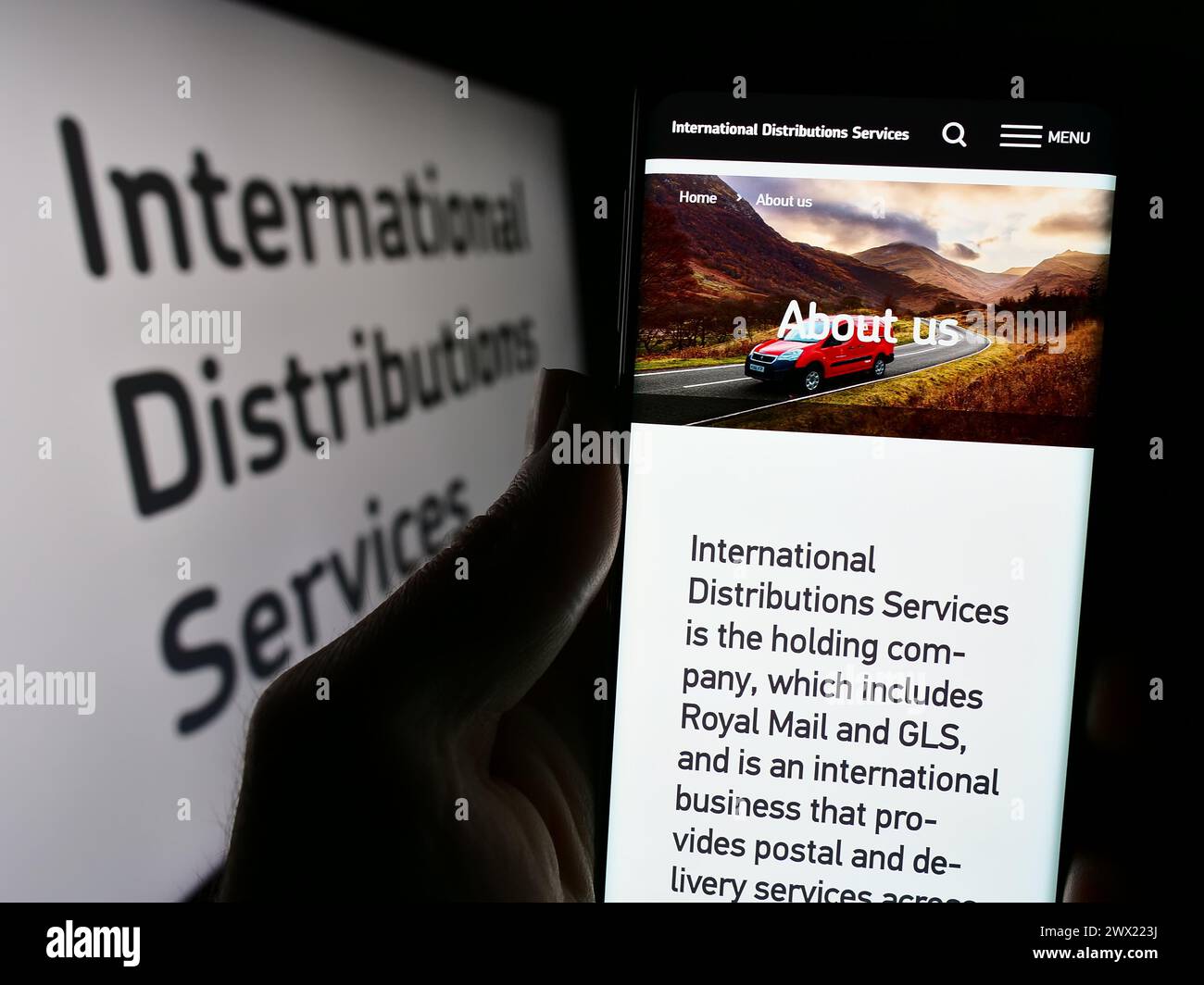 Person holding cellphone with webpage of British company International Distributions Services plc with logo. Focus on center of phone display. Stock Photo