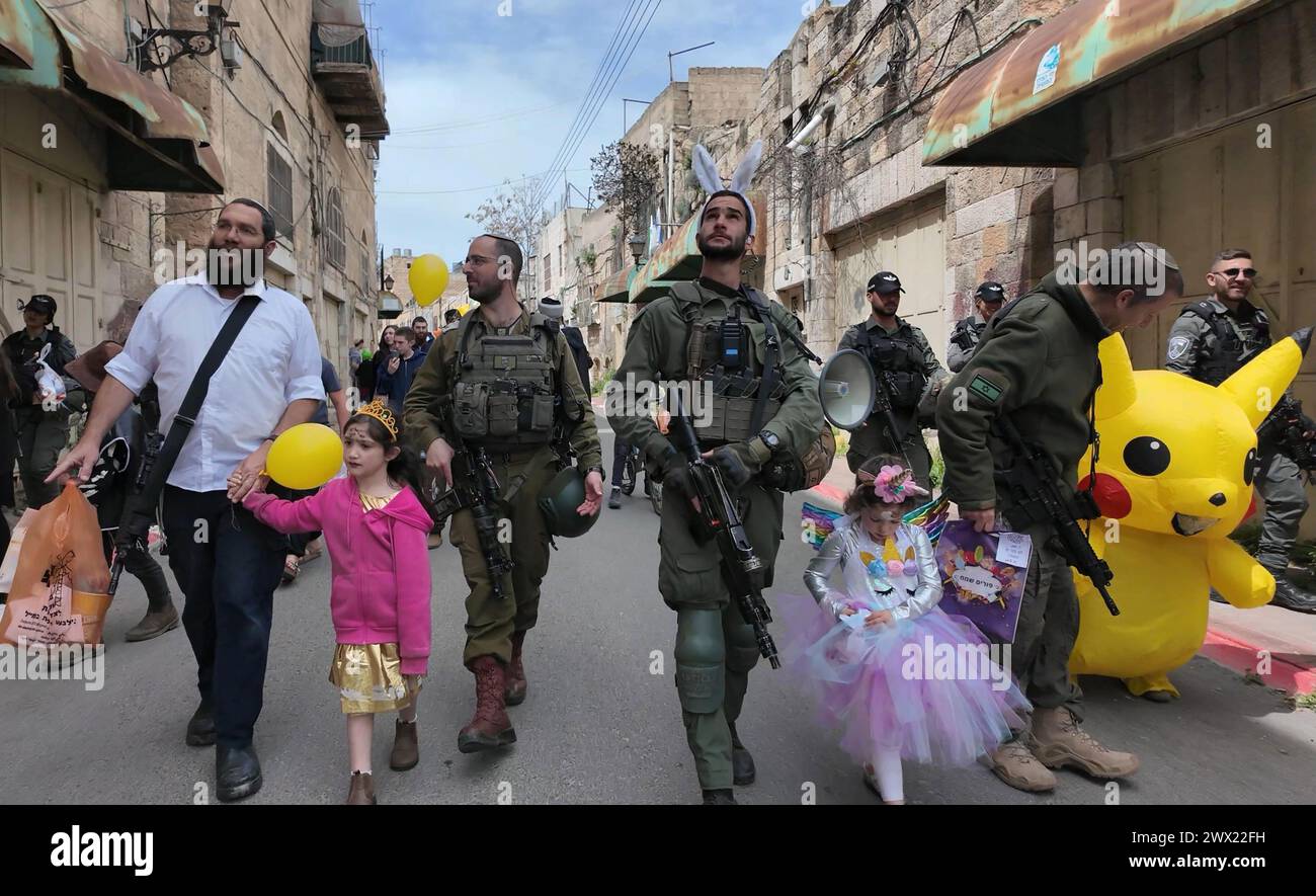 Jewish settlers wearing costumes march down Al-Shuhada street, which is largely closed to Palestinians, during the annual Purim parade as Israeli security forces secure the celebrations on March 24, 2024 in Hebron, Israel. Stock Photo