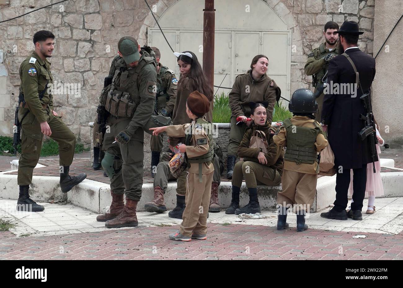 Israeli children in military costume stand amid members of Israeli security forces as Jewish settlers march during the annual Purim parade on March 24, 2024 in Hebron, Israel. Stock Photo