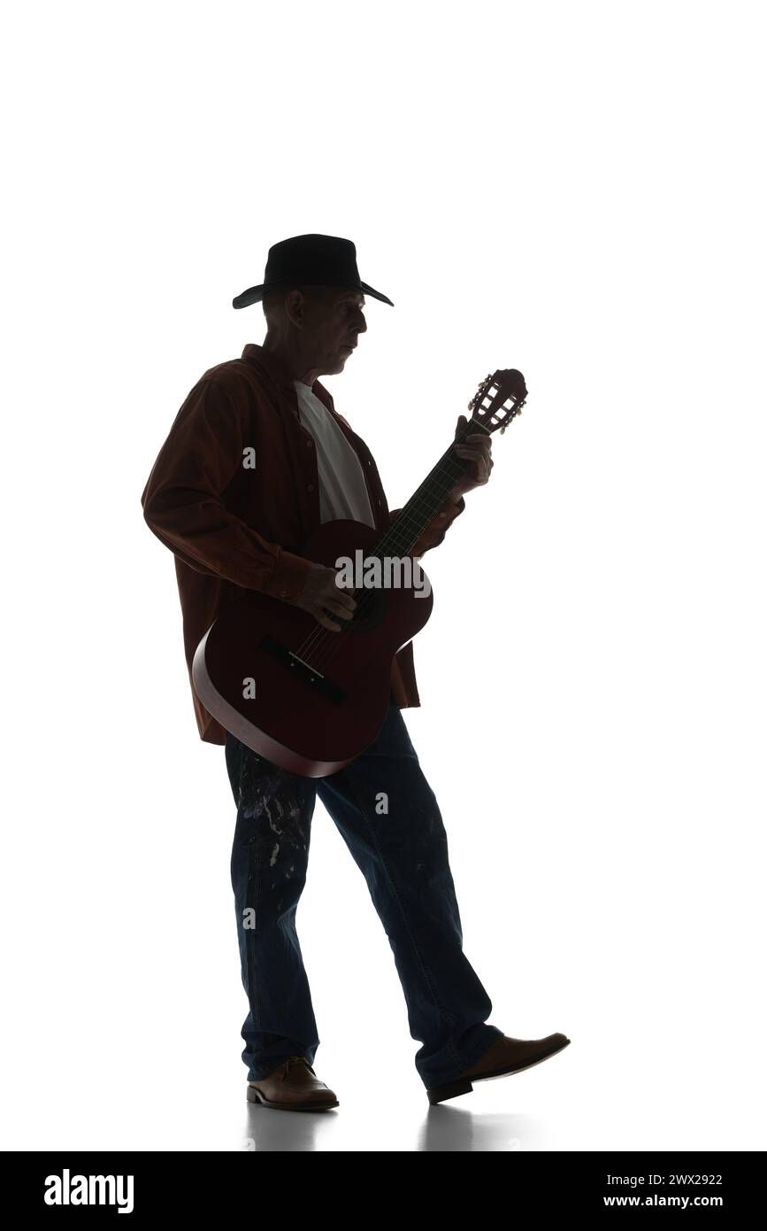 Silhouette of man in fedora hat playing guitar, performing isolated on white background. Black and white image. Stock Photo