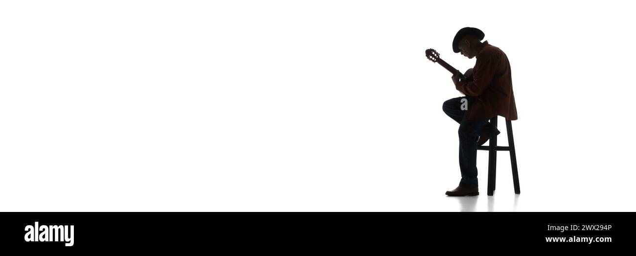 Man in fedora hat sitting on chair and playing guitar on white background. Black and white image. Stock Photo