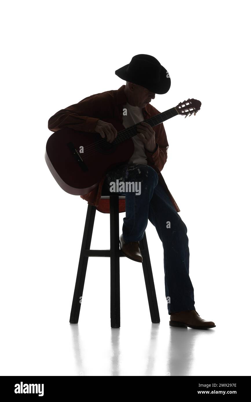 Man in fedora hat sitting on chair and playing guitar on white background. Black and white image. Solo performer. Stock Photo