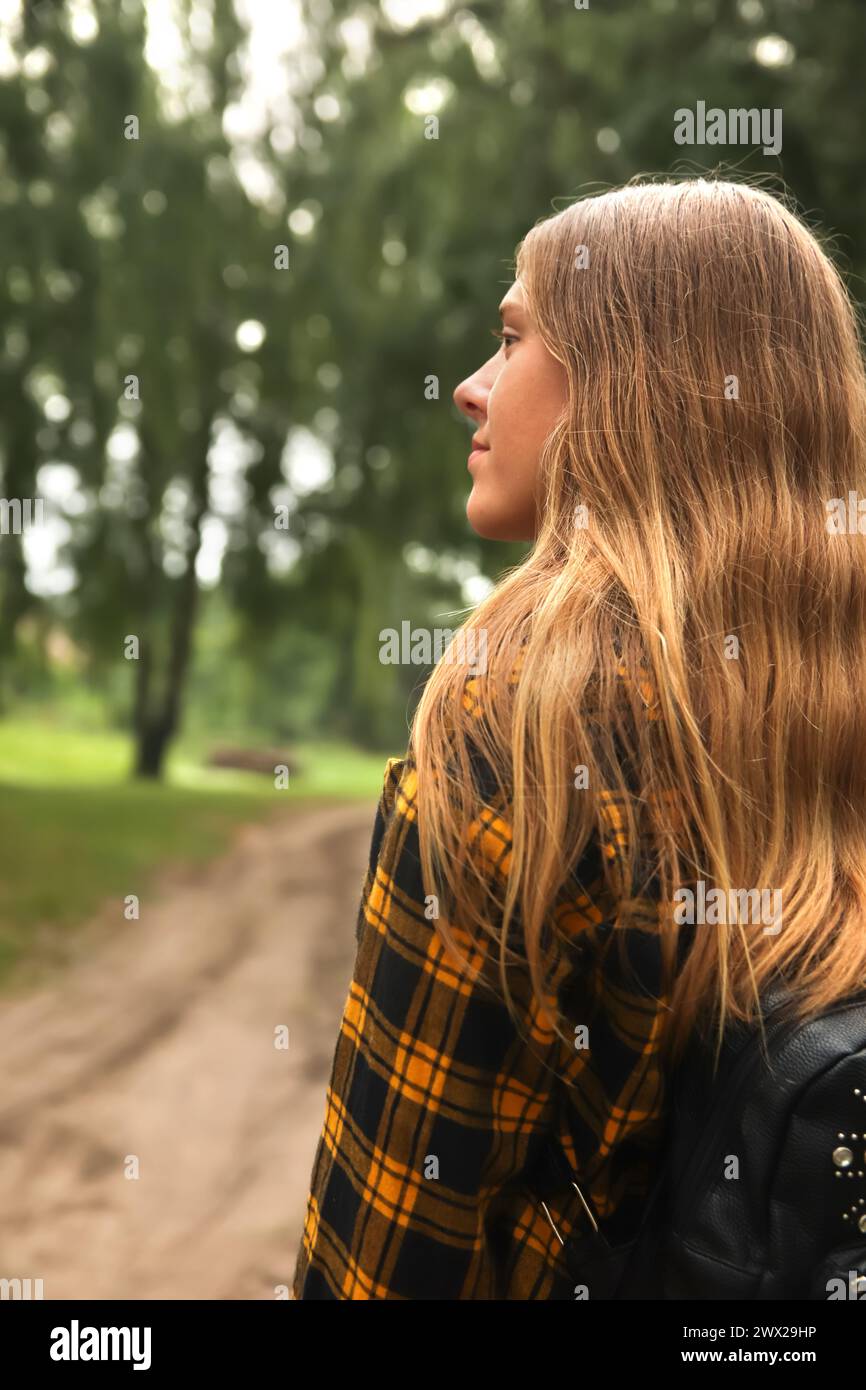 Teen girl outdoors. Backpack woman. Hipster girl with backpack in woods. Traveler background. Tourist summer lifestyle. Blurred. Blonde curly hair. Te Stock Photo