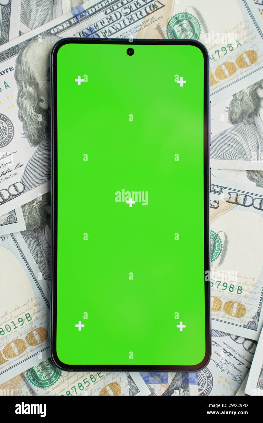 Smartphone with green screen on pile of dollar banknotes, top view. Concept of online earnings Stock Photo
