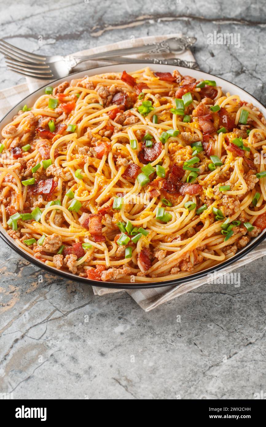 Western Cowboy Spaghetti with the addition of Ground beef, bacon, cheddar cheese, onion and hot sauce closeup on the plate on the table. Vertical Stock Photo