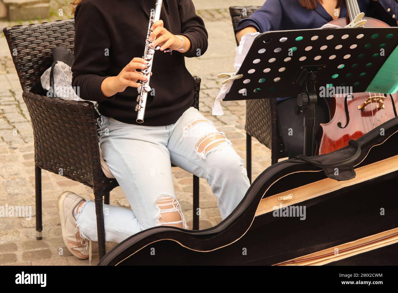 A closeup plane of street orchestra flautist with flute in her hands. Street music band performing on old city background. Close up women playing flut Stock Photo