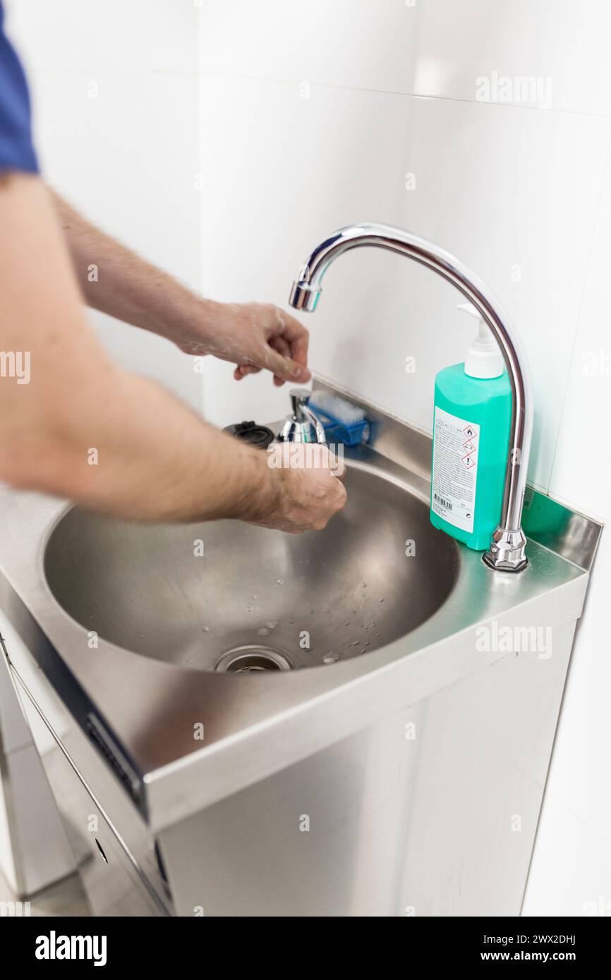 veterinary man surgeon in epi clothes preparing to operate washing hands in clinic sink Stock Photo