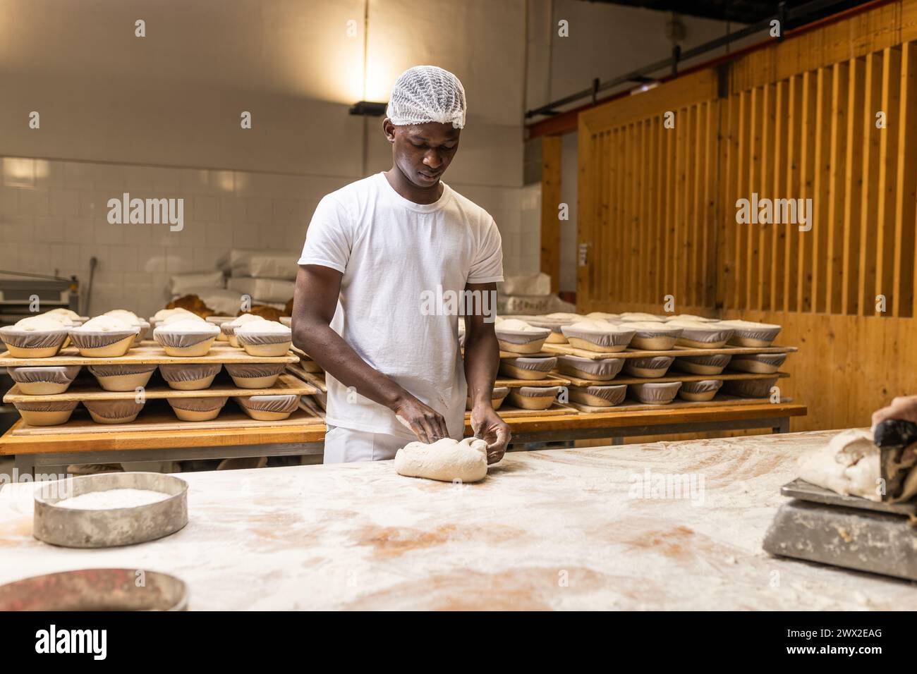 young black male apprentice, kneading bread dough on the bakery school's workbench Stock Photo