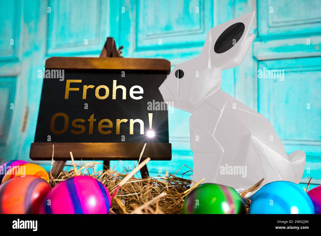 March 27, 2024: Easter greetings: Happy Easter Text on a plaque next to an Easter bunny in straw with Easter eggs. PHOTOMONTAGE *** Ostergruß: Frohe Ostern Text auf einer Tafel neben einem Osterhasen in Stroh mit Ostereiern. FOTOMONTAGE Stock Photo