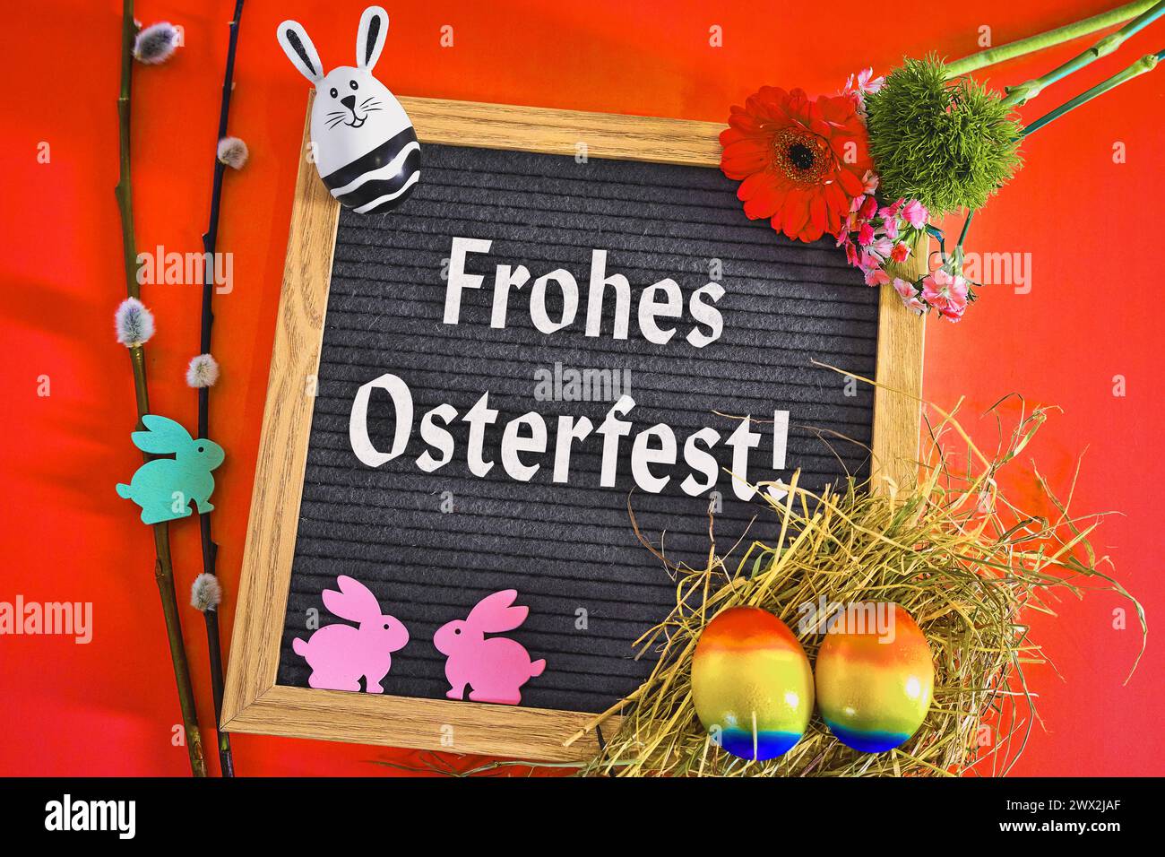 March 27, 2024: Greetings: Happy Easter Text on a board surrounded by Easter decorations on a red background. PHOTOMONTAGE *** Gruß: Frohes Osterfest Text auf einer Tafel umgeben von Osterdekoration auf rotem Hintergrund. FOTOMONTAGE Stock Photo