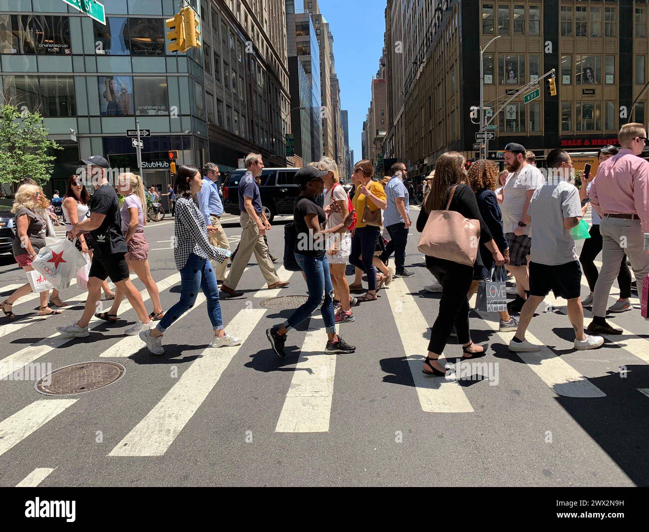 Pedestrians and travelers walk and cross the street using the crosswalk during lunch time in New York City Stock Photo