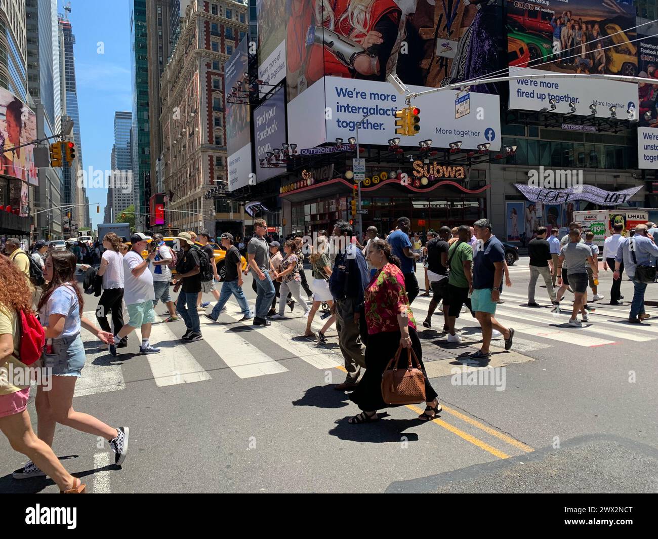 Pedestrians are surrounded by video billboards as they cross the street at the crosswalk in New York City’s Times Square Stock Photo