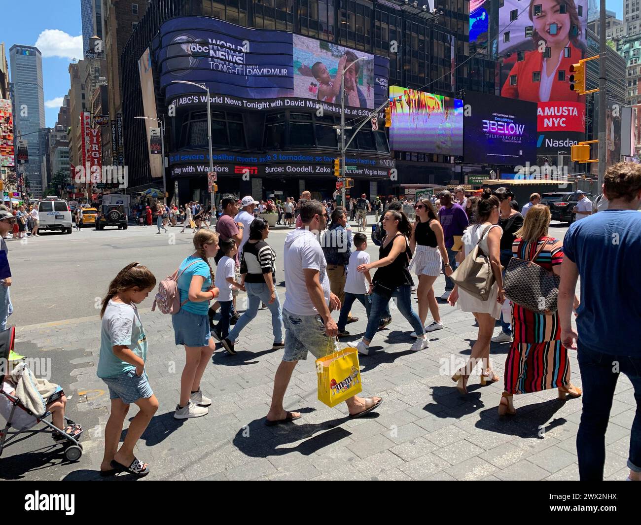 A large crowd of tourists and families walk across the street in New York's Times Square Stock Photo