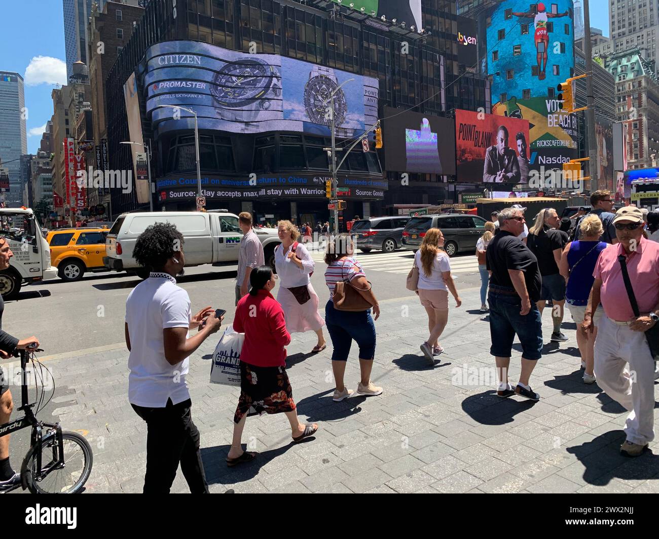 On a sunny summer day, pedestrians walk across the street in New York City's Times Square Stock Photo
