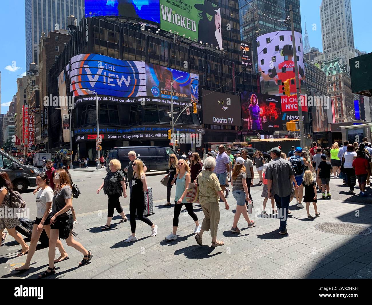 A crowd of people cross the street in the heart of New York City Times Square, surrounded by the billboards and advertisements Stock Photo