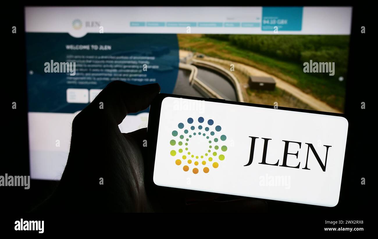 Person holding smartphone with logo of company JLEN Environmental Assets Group Limited in front of website. Focus on phone display. Stock Photo