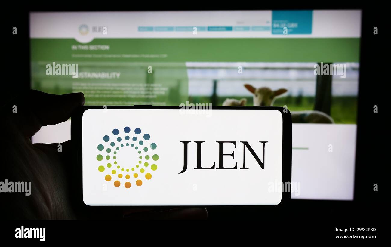 Person holding cellphone with logo of company JLEN Environmental Assets Group Limited in front of business webpage. Focus on phone display. Stock Photo