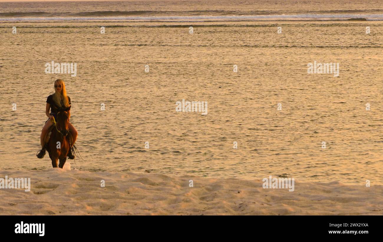 A woman riding a horse on the beach at sunset Stock Photo