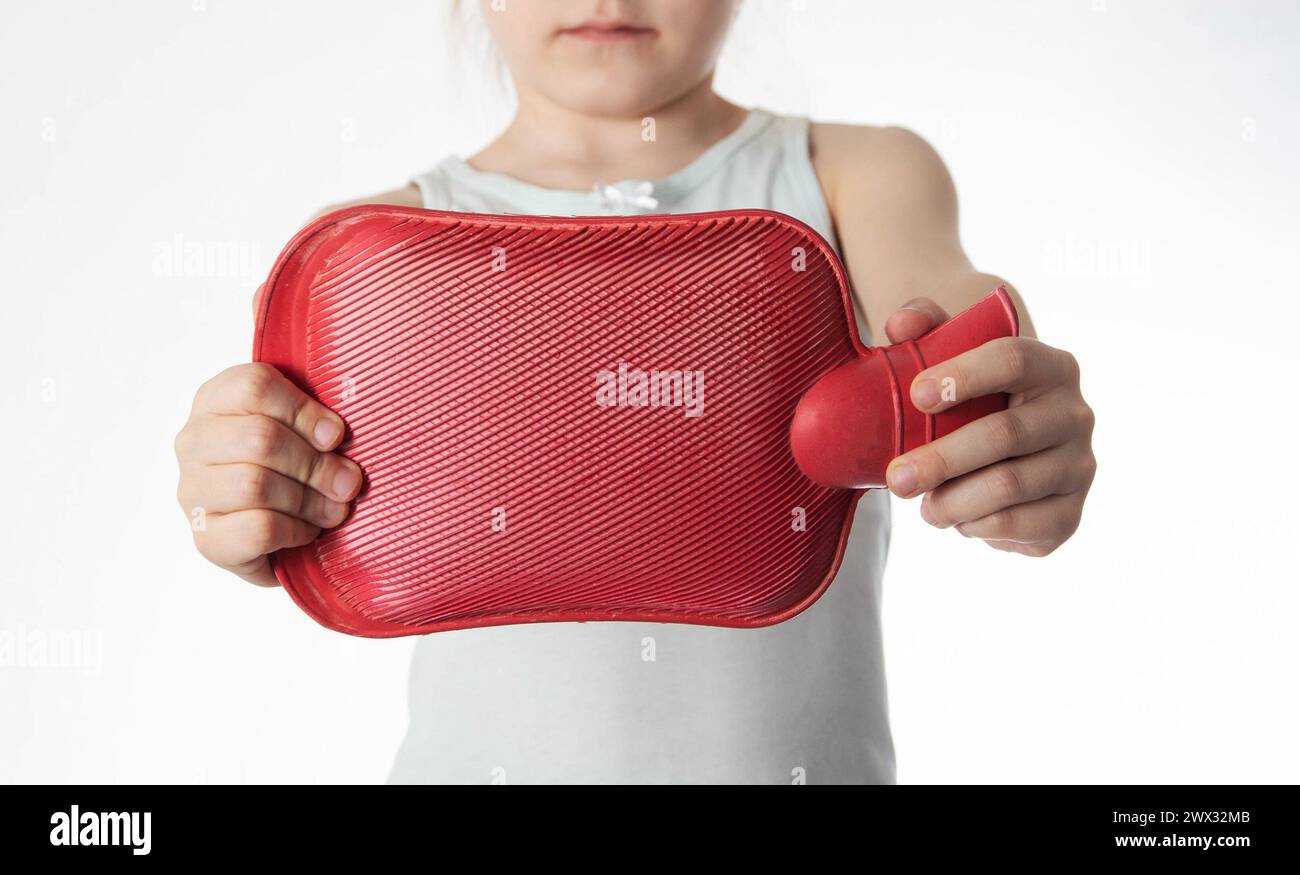 The girl holds a red heating pad with warm water in her hands at outstretched arms. Concept for heat treatment of muscle spasms and pain. Stock Photo