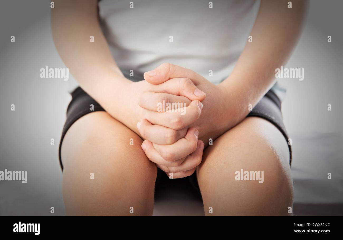 The girl's hands are folded on her knees, close-up. Bullying concept at school, sadness Stock Photo