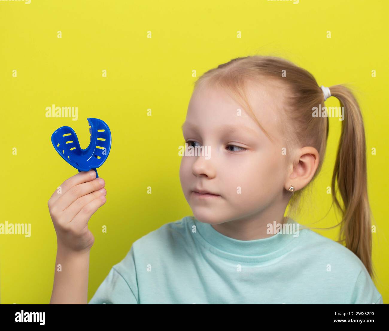 A seven year old girl looks at a blue dental impression tray in