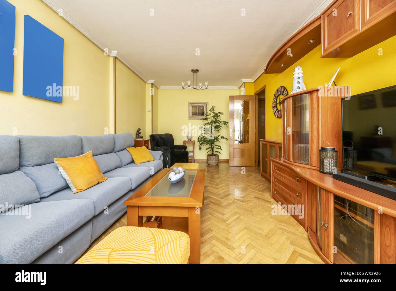 Conventional living room with a long green fabric sofa, a wooden sideboard and walls painted in various shades of yellow Stock Photo