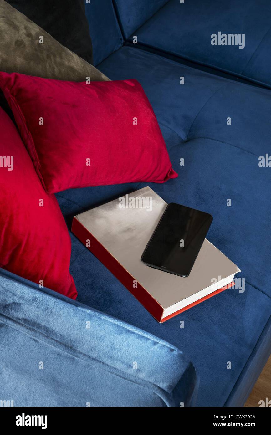 A blue velvet sofa with a book and a mobile phone on the seat Stock Photo