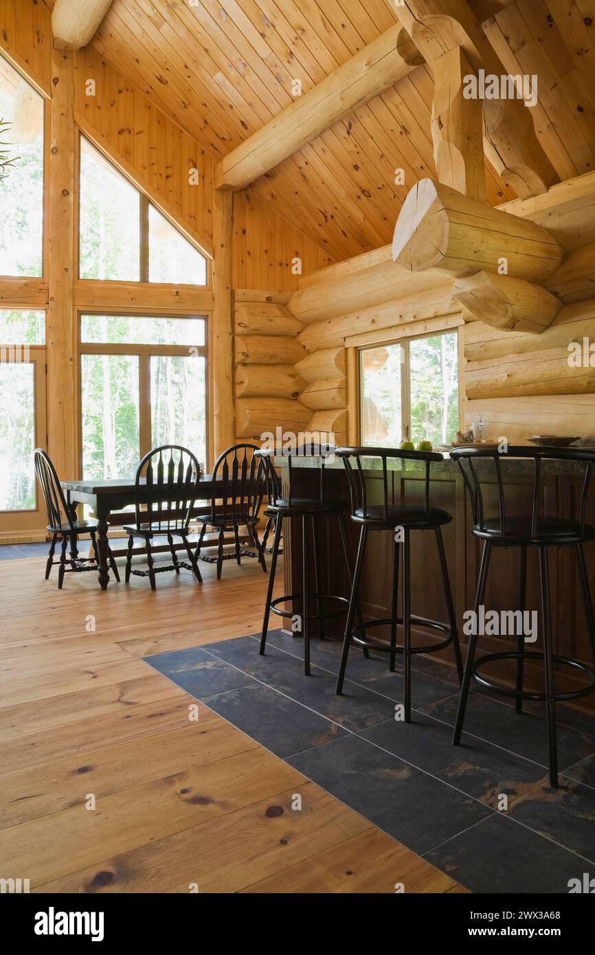 Island with dark grey granite countertop and black stained wooden bar stools plus antique table with rounded high back chairs in open concept kitchen Stock Photo