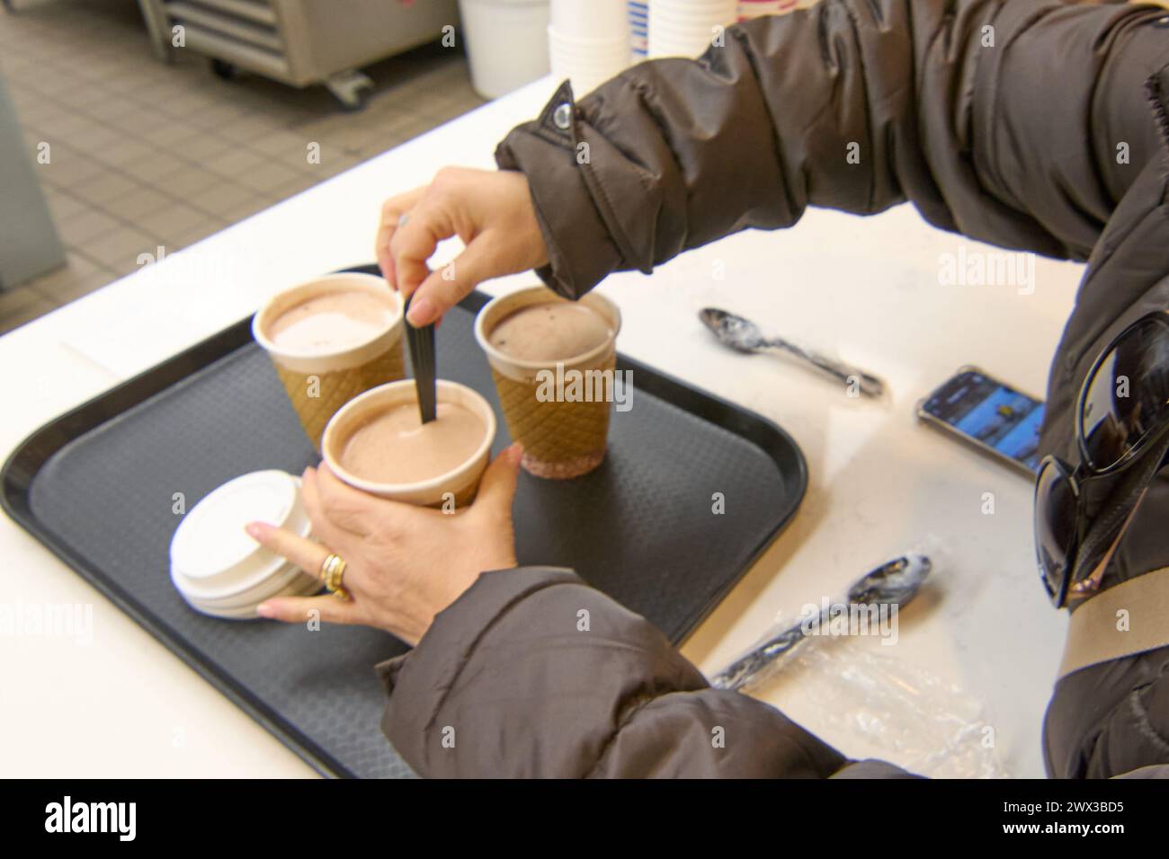 A hand clutches a tray with three cups of coffee to go in a coffee shop, symbolizing the convenience and efficiency of service in urban life. Stock Photo