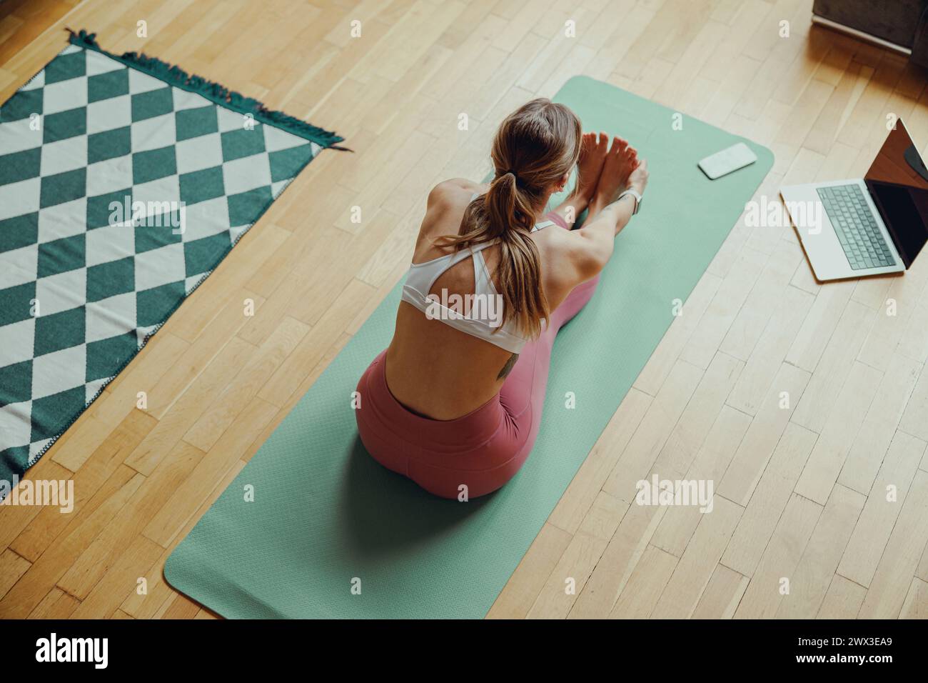 A woman sits on a yoga mat on hardwood flooring in her living room ...