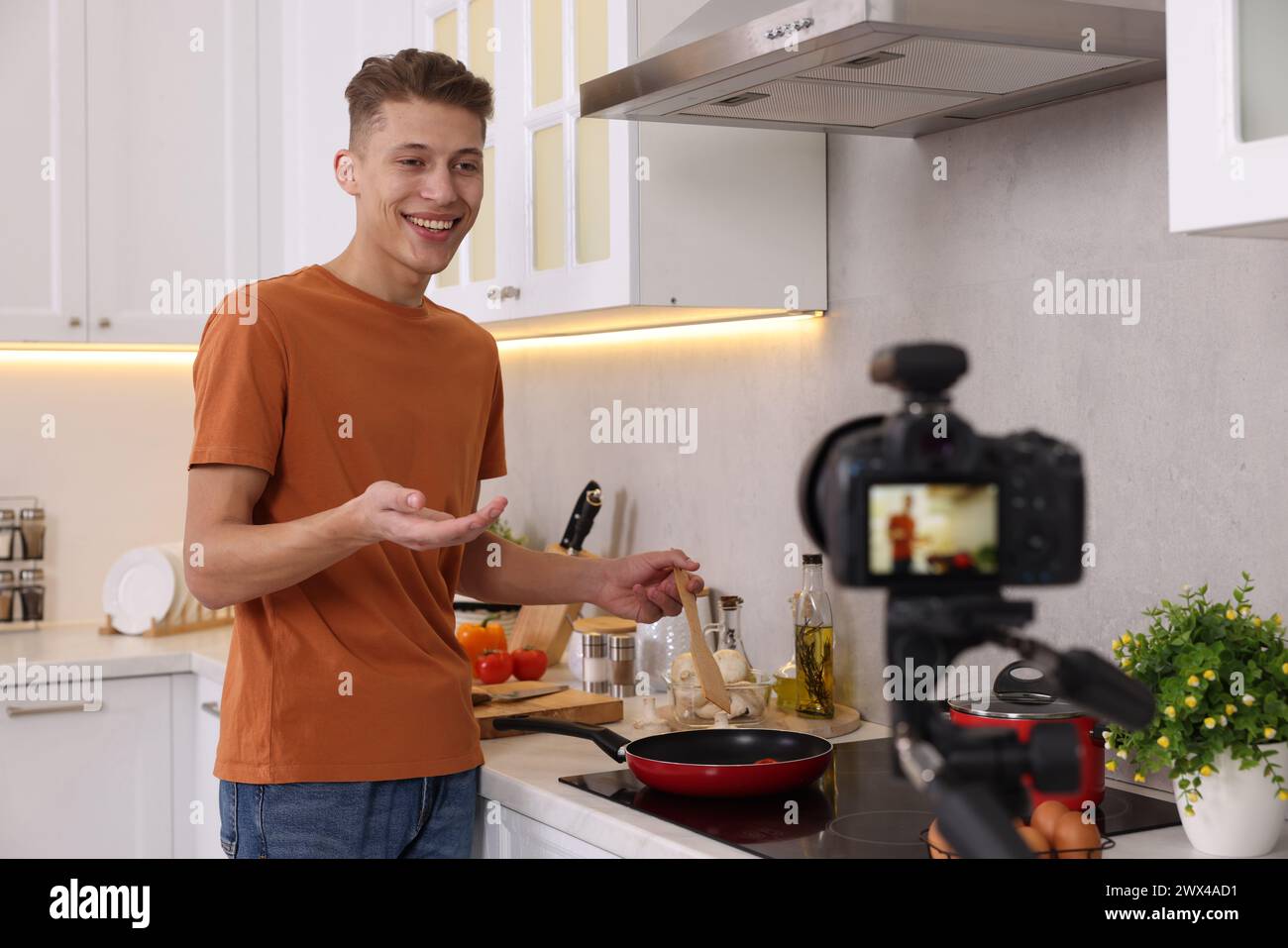Smiling food blogger explaining something while recording video in kitchen Stock Photo