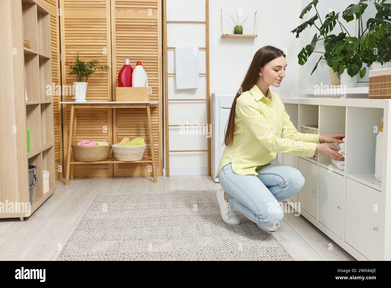Beautiful young woman taking towels from drawer in laundry room Stock