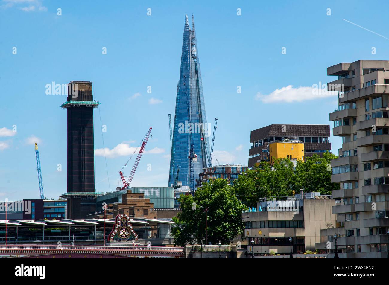 The Shard pierces the London skyline, flanked by construction cranes and modern architecture along the bustling River Thames Stock Photo