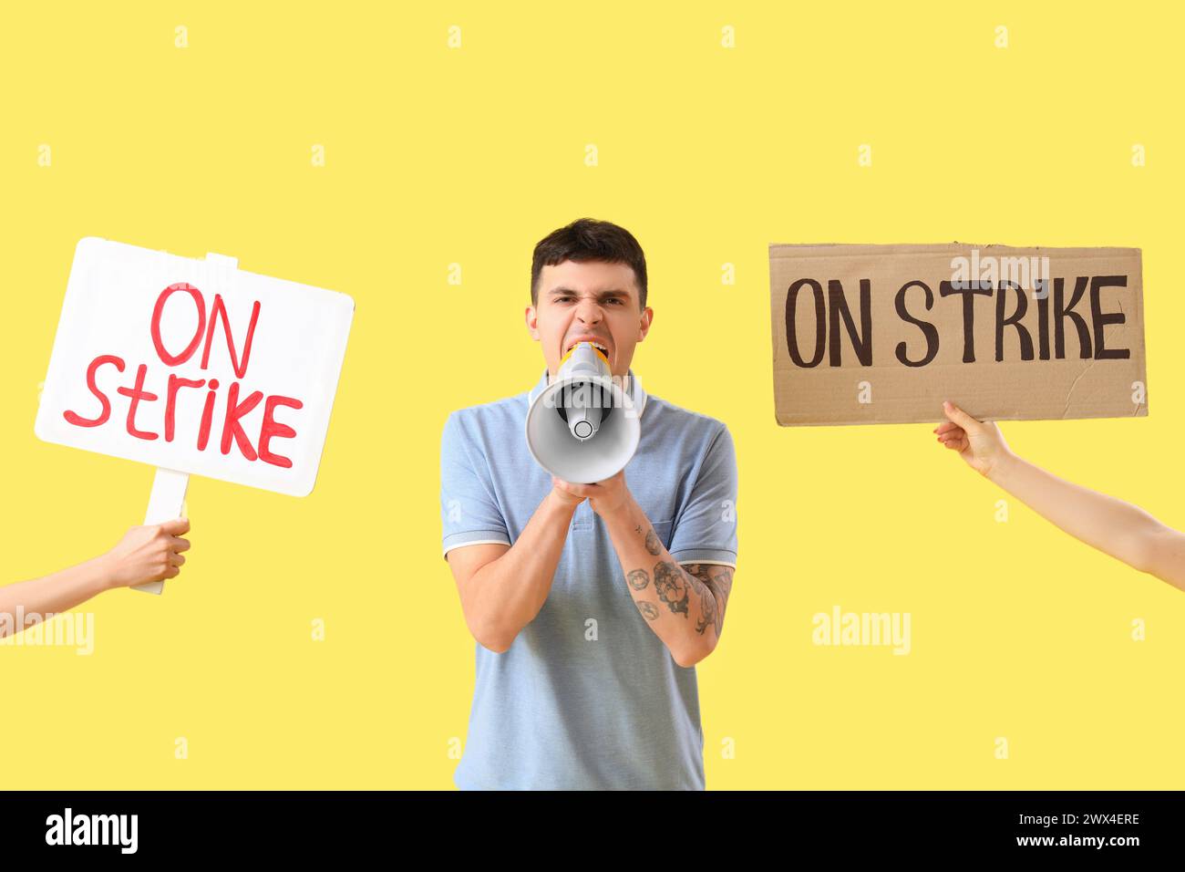 Protesting young man shouting into megaphone and placards with text ON STRIKE against yellow background Stock Photo