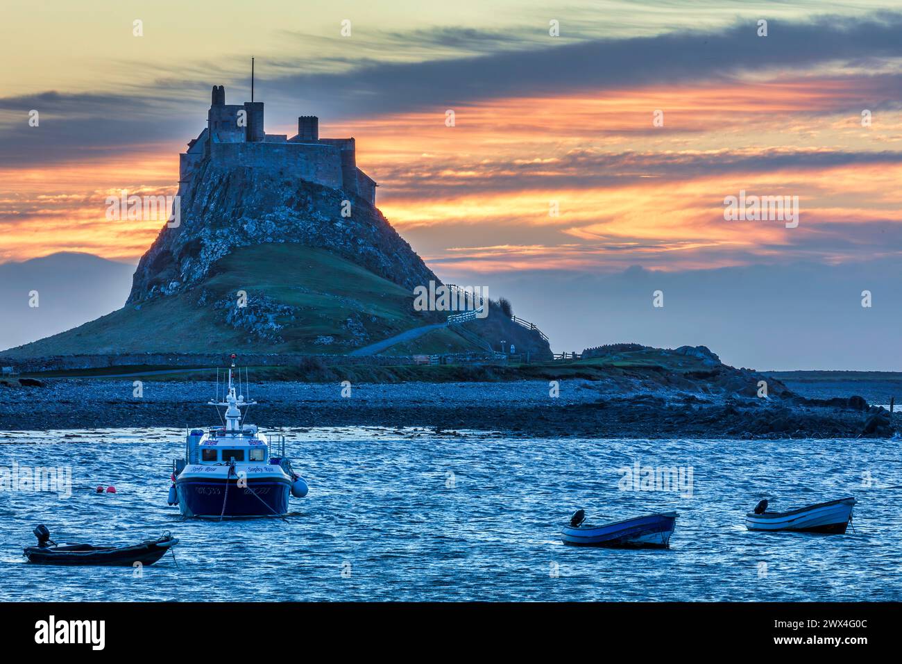 A view at dawn of Lindisfarne Castle viewed from the harbour with moored boats in the foreground on Holy Island in Northumberland Stock Photo
