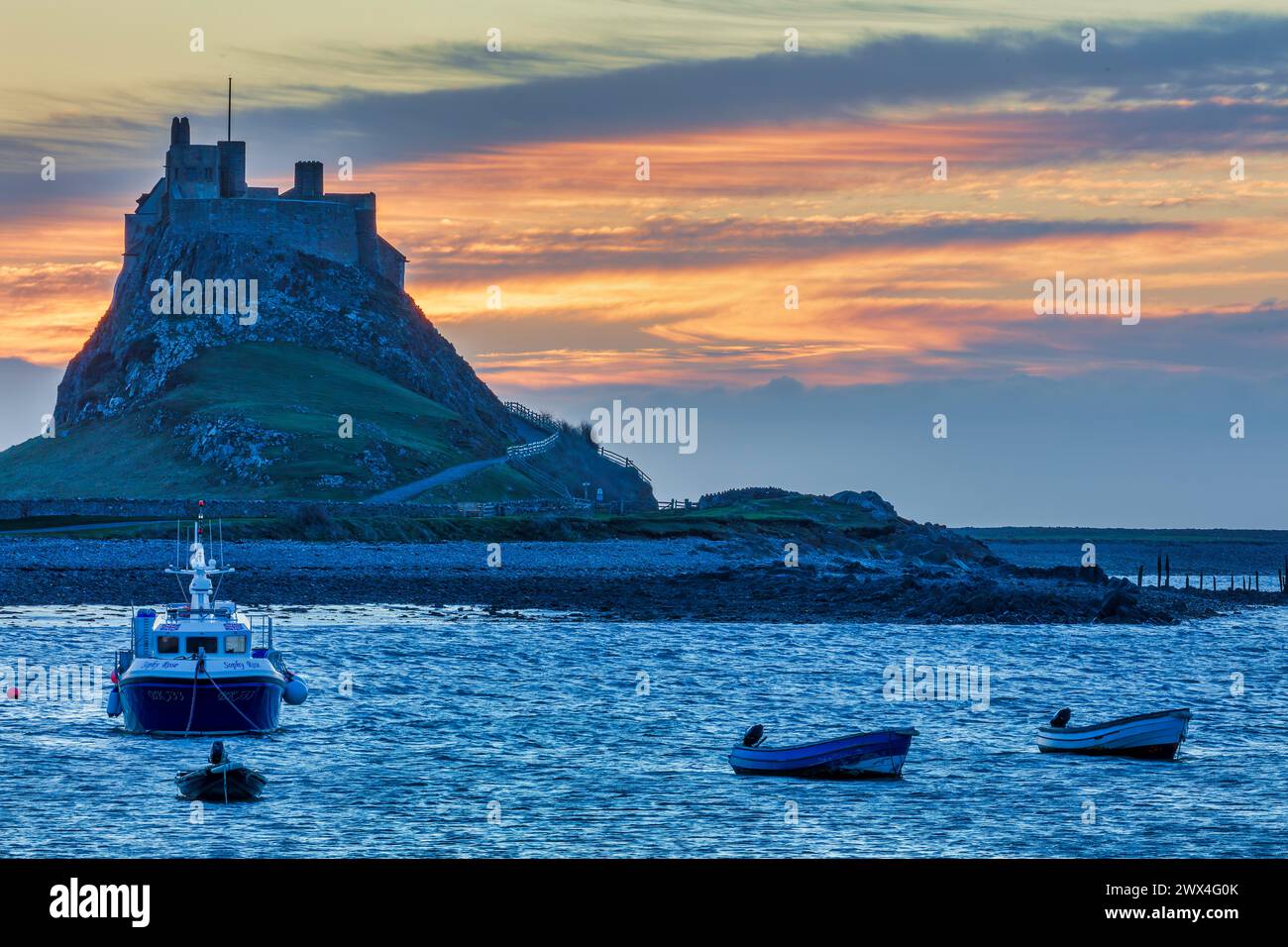 A view at dawn of Lindisfarne Castle viewed from the harbour with moored boats in the foreground on Holy Island in Northumberland Stock Photo