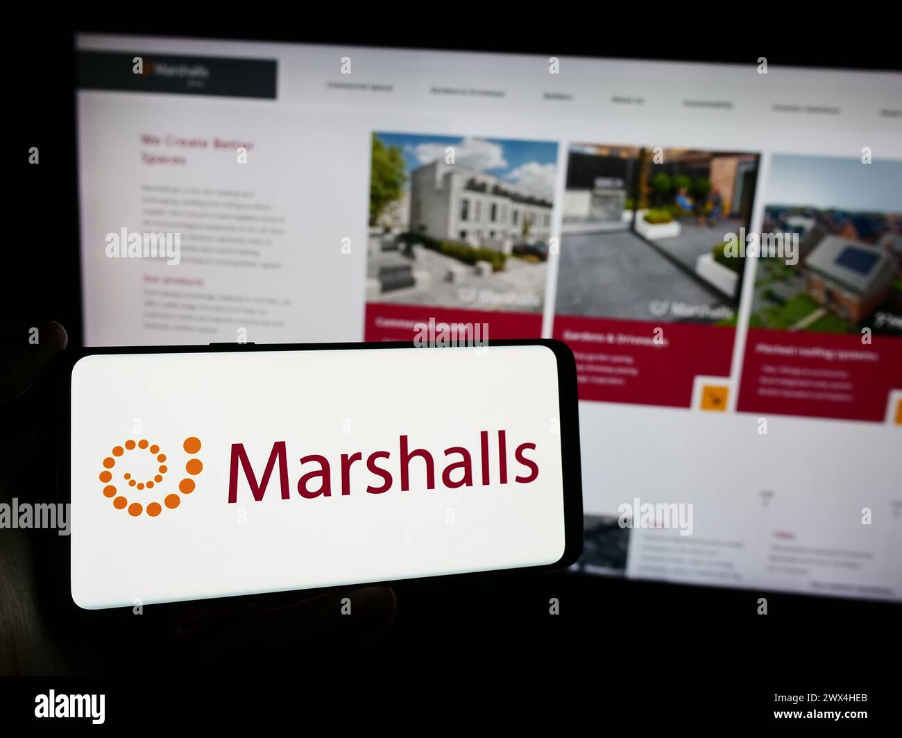 Person holding cellphone with logo of British landscaping products company Marshalls plc in front of business webpage. Focus on phone display. Stock Photo